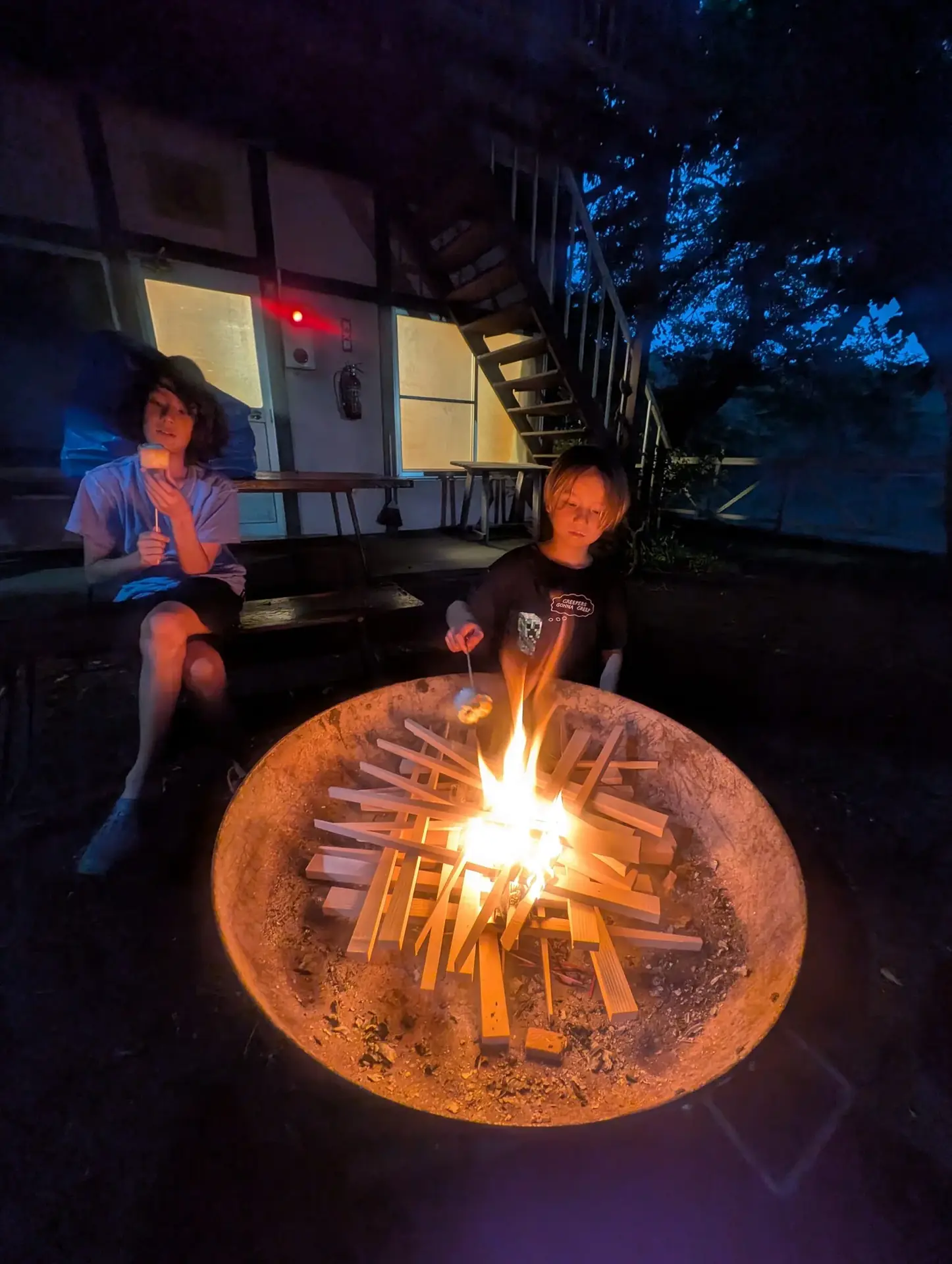 Campers gathered around um bright campfire em noite outside um cabin