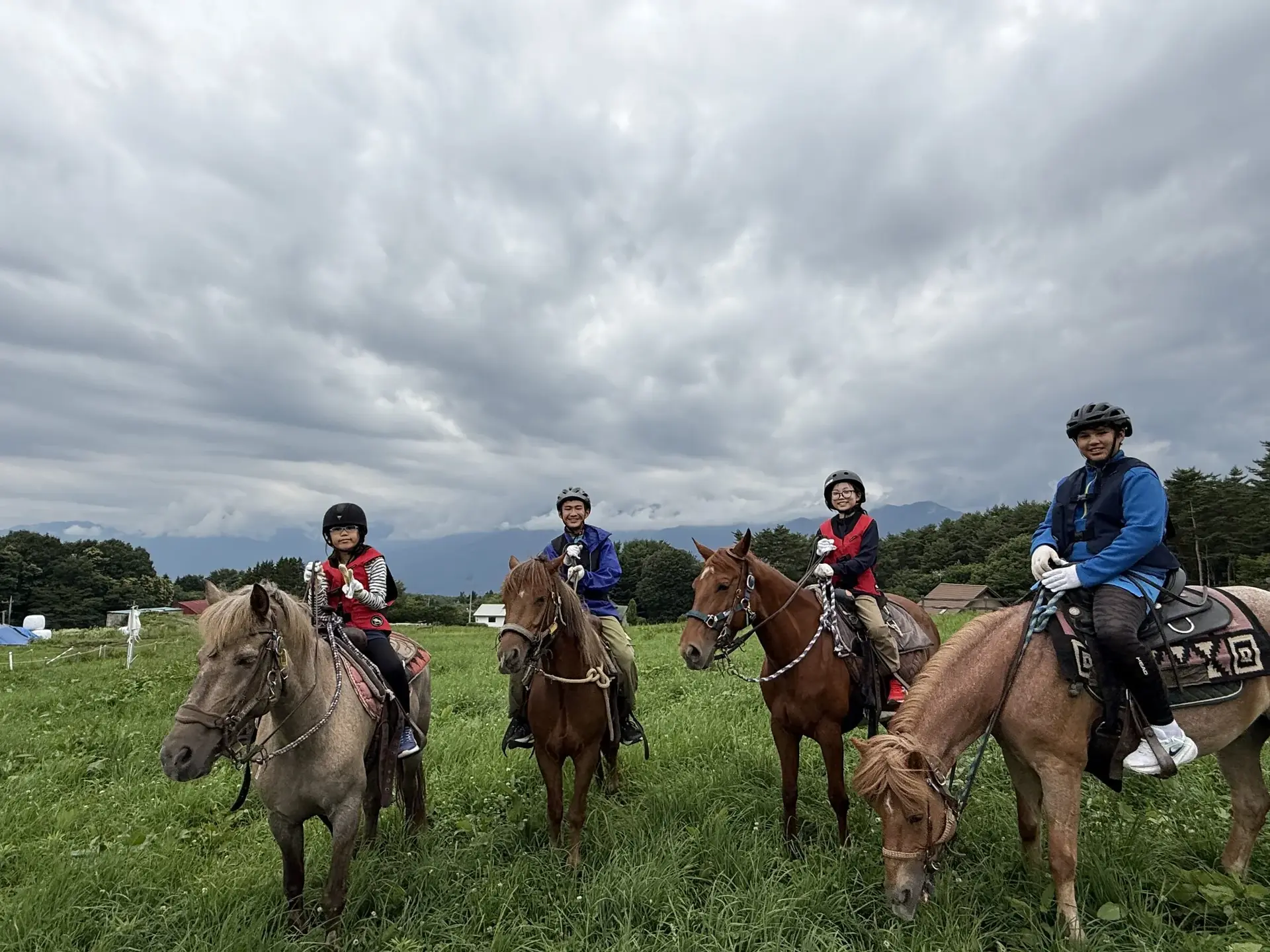 Helmeted participantes riding horses por toda um aberto gramado campo com montanhas além